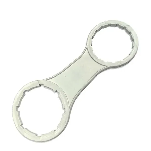 Llave abre garrafas de color claro, colocada en diagonal, con dos aros dentados de distinto tamaño unidos por un mango plano.