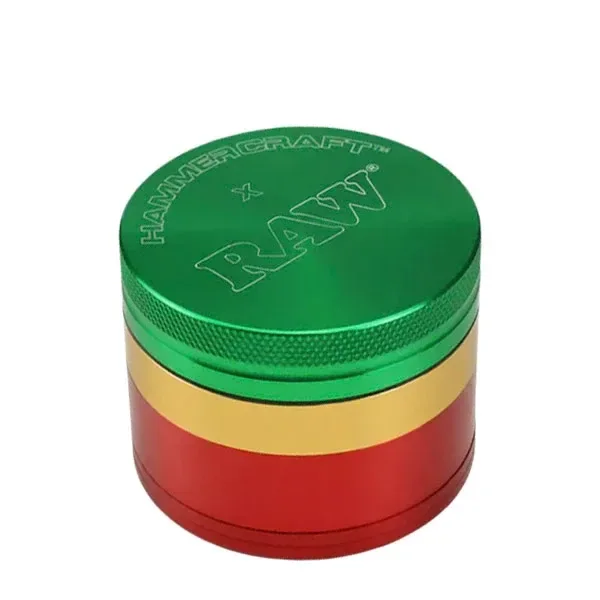 Grinder RAW cerrado, de cuerpo cilíndrico con franjas verde, amarilla y roja, tapa grabada y borde estriado sobre fondo blanco.
