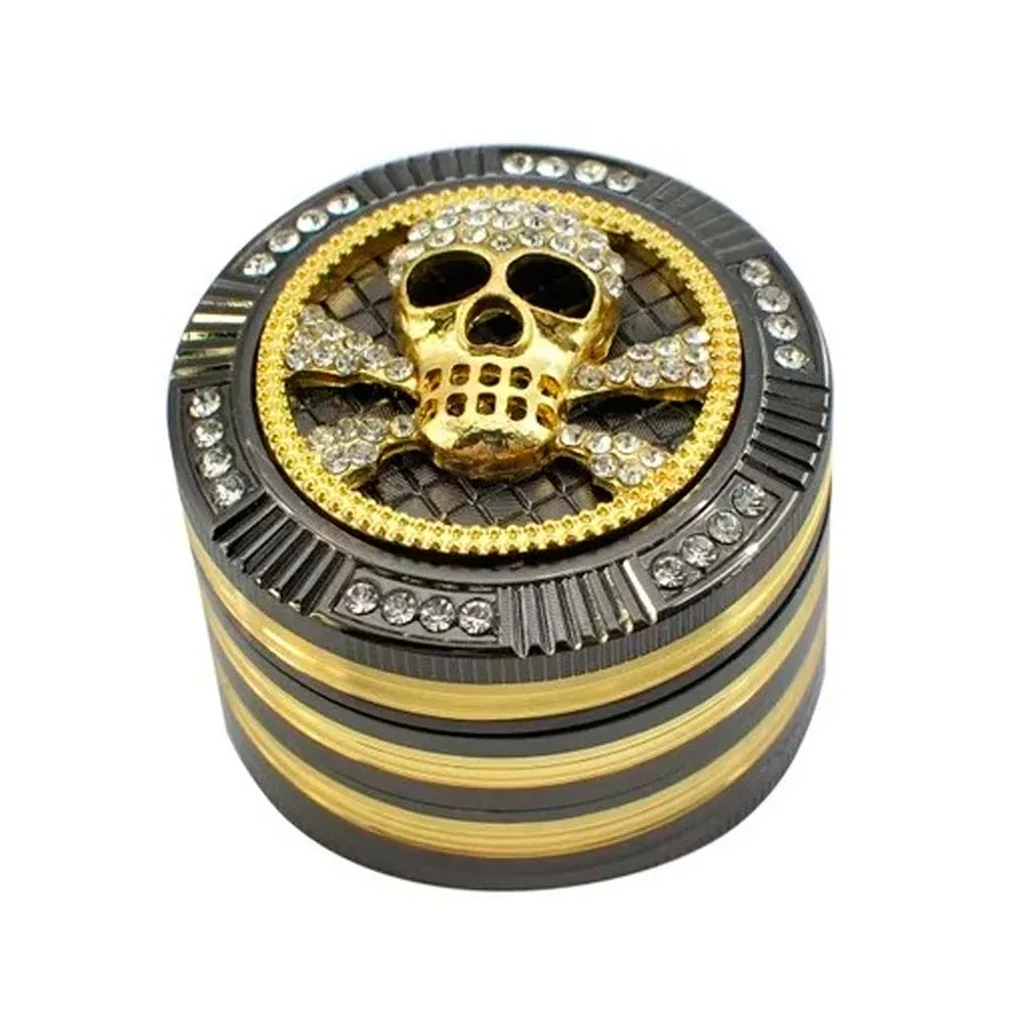 Grinder cilíndrico negro y dorado, con calavera y tibias cruzadas en relieve y adornos brillantes en la tapa, visto en perspectiva.