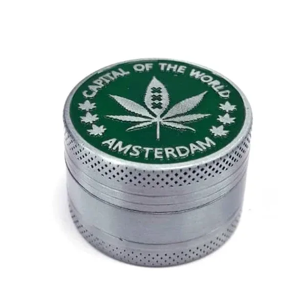 Grinder metálico plateado con bordes texturizados y tapa verde decorada con una hoja de cannabis y el texto «Amsterdam».