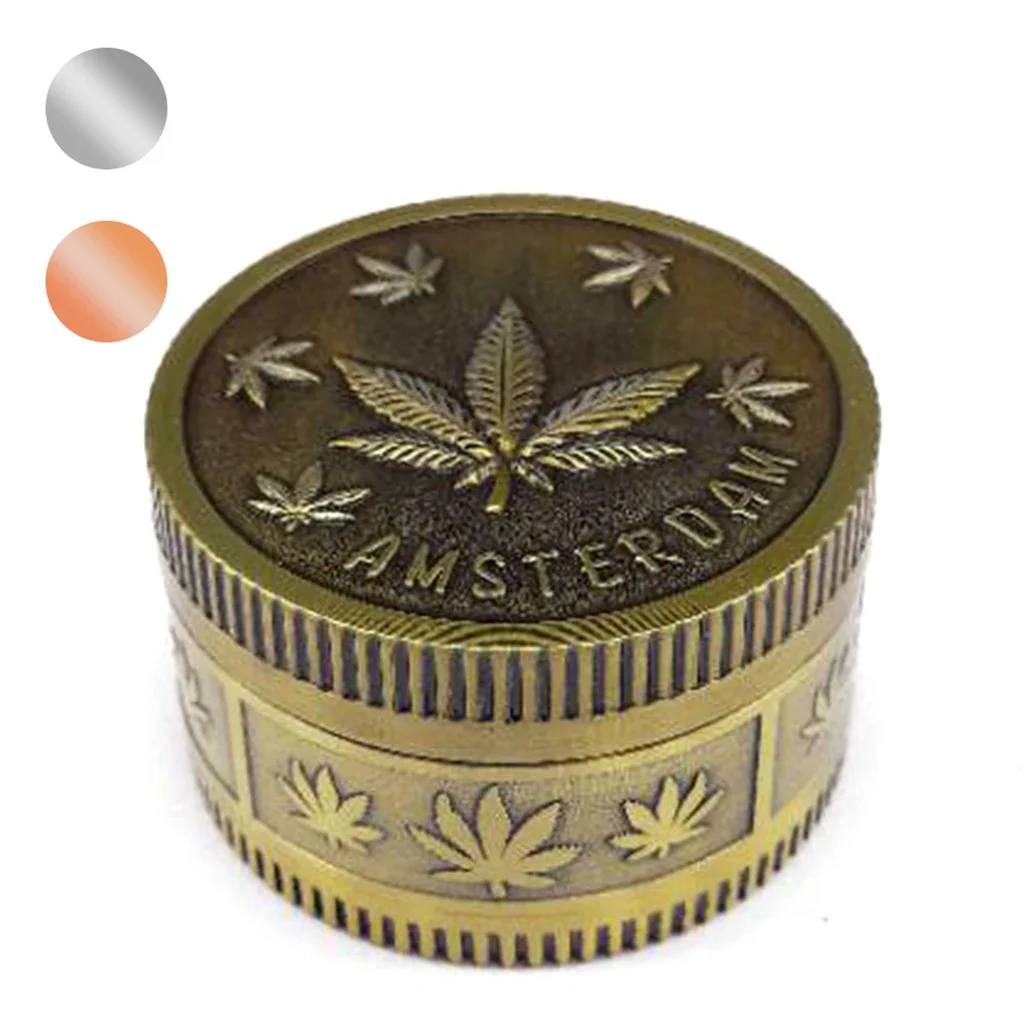 Grinder de tono dorado envejecido con hojas de cannabis en relieve, inscripción Amsterdam y bordes estriados; muestras de color al lado.