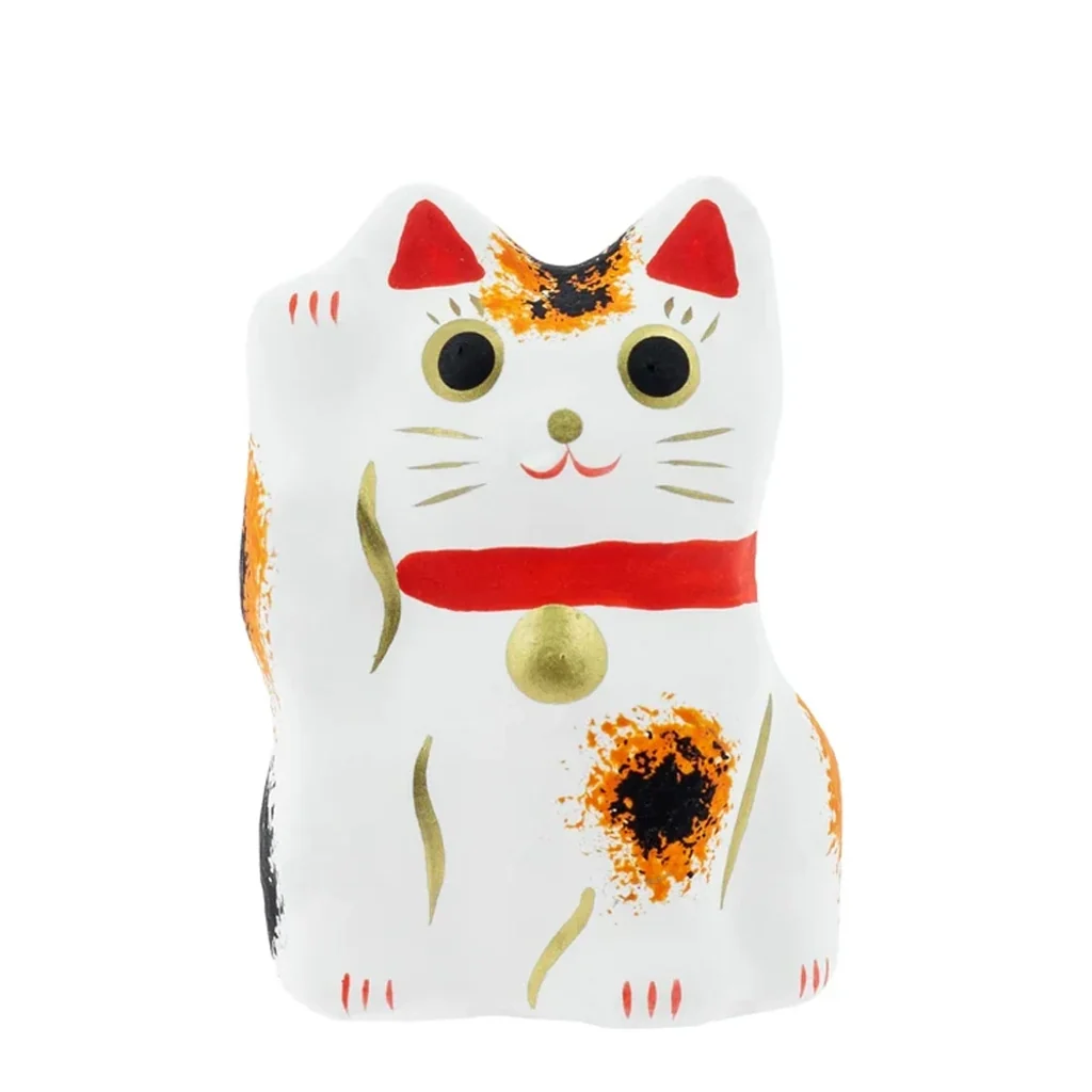 Figura Maneki Neko blanca con manchas naranjas y negras, una pata levantada, collar rojo y detalles dorados sobre fondo blanco. Figura Maneki Neko blanca con manchas naranjas y negras, una pata levantada, collar rojo y detalles dorados sobre fondo blanco.