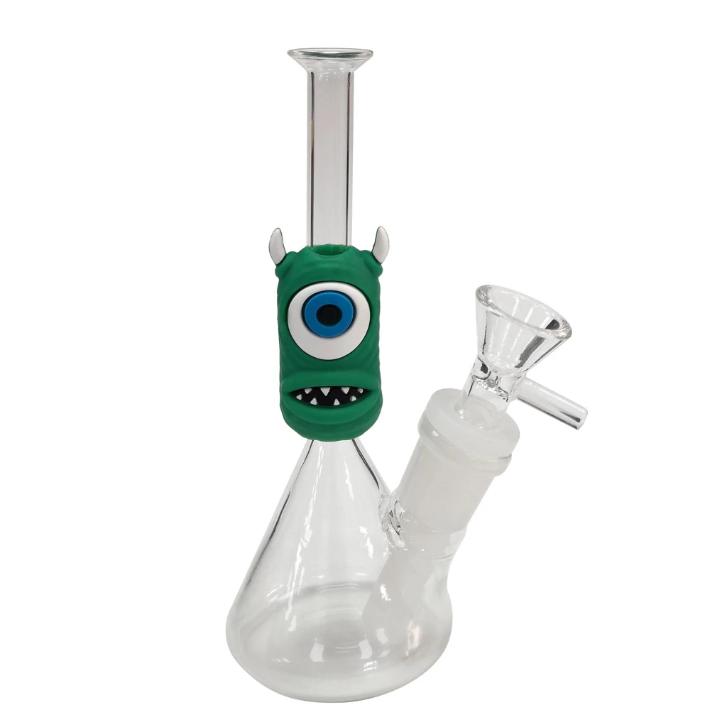 Bong transparente con base ancha, cazoleta lateral y funda verde de monstruo con un gran ojo azul, cuernos blancos y dientes puntiagudos.