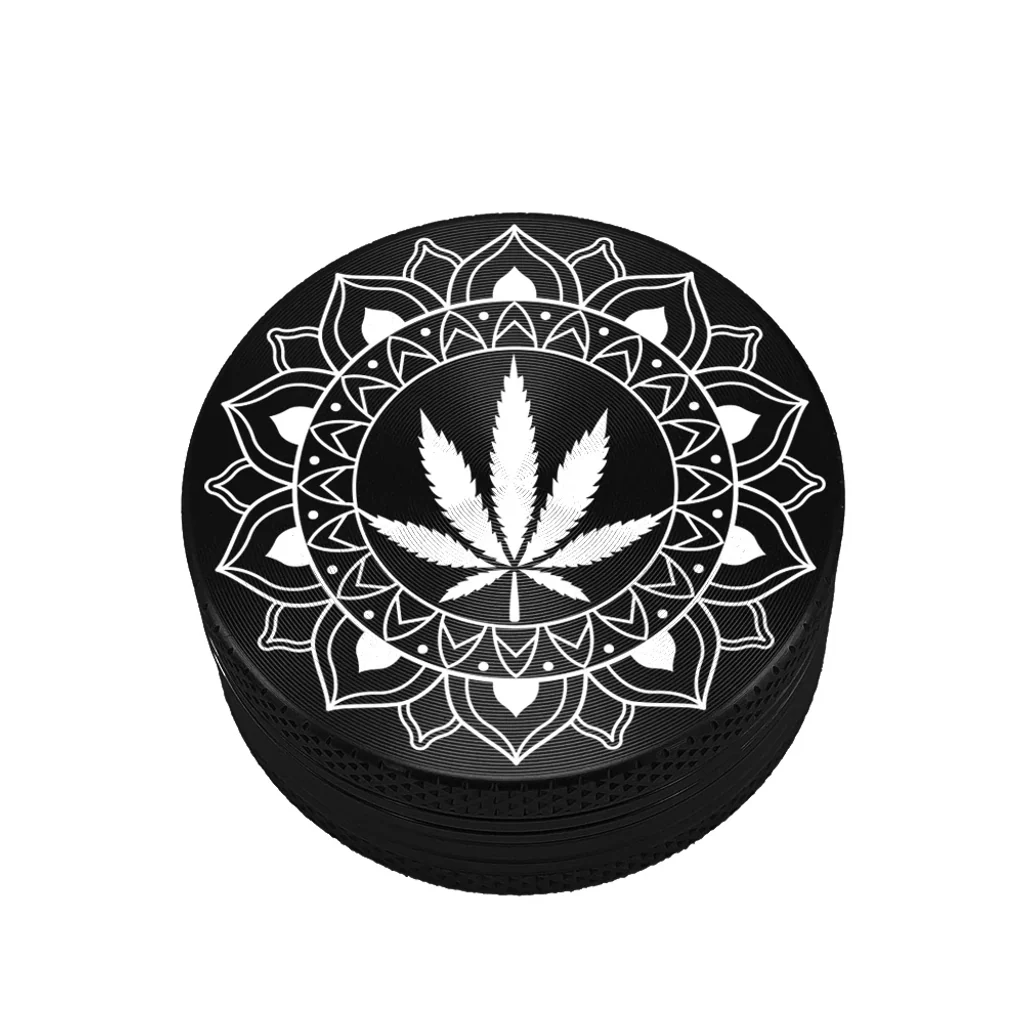 Grinder negro Design Tribal Leaf visto en perspectiva, con una hoja de cannabis blanca rodeada de un mandala y bordes texturizados.