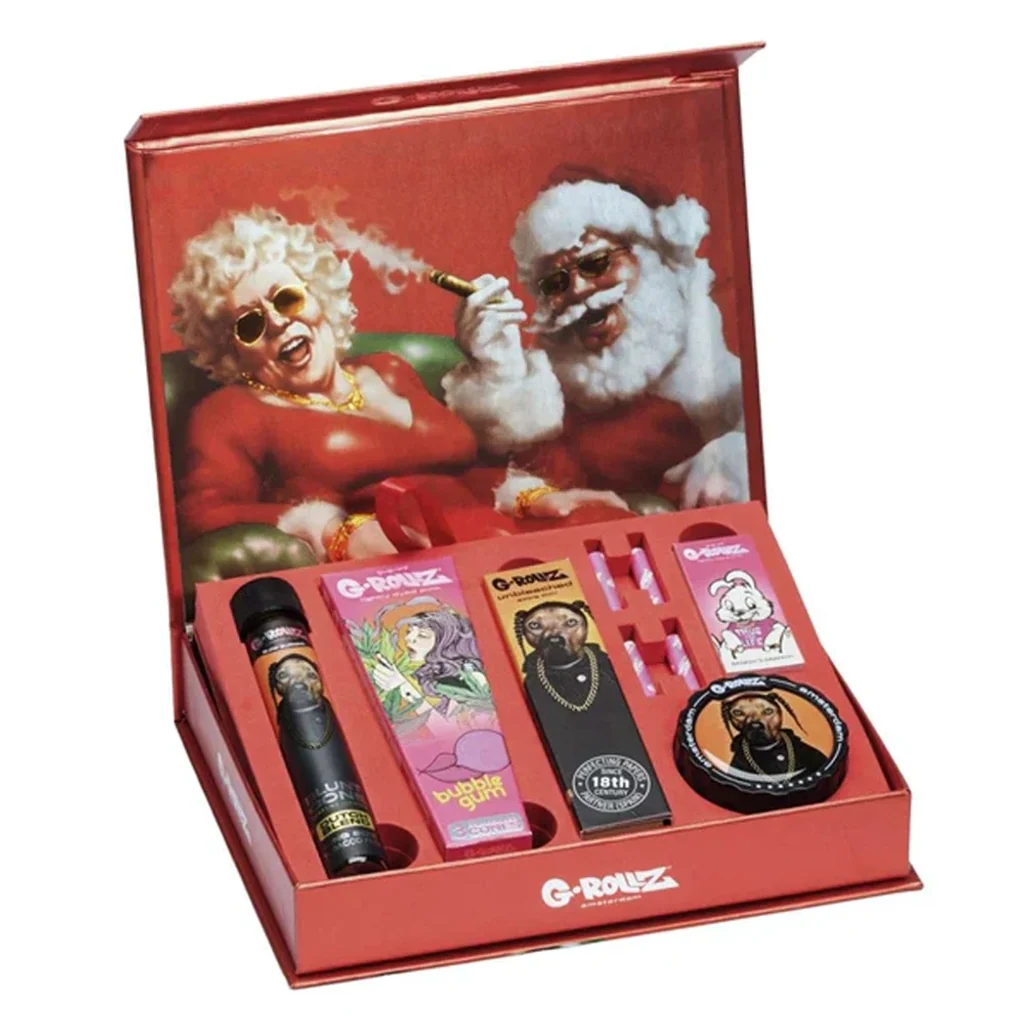 Caja roja G-Rollz abierta con accesorios en compartimentos y una ilustración navideña de personajes con gafas de sol en la tapa. Caja roja G-Rollz abierta con accesorios en compartimentos y una ilustración navideña de personajes con gafas de sol en la tapa.