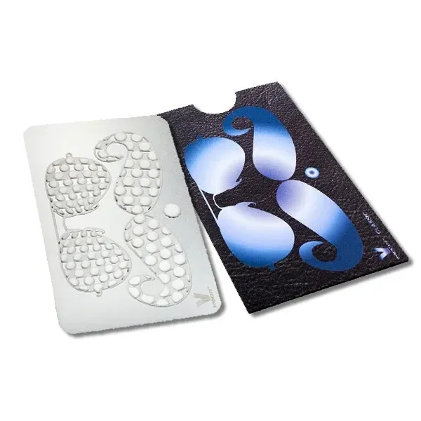 Grinder de tarjeta plateado con perforaciones en forma de bigote, junto a una funda negra decorada con bigotes azules. Grinder de tarjeta plateado con perforaciones en forma de bigote, junto a una funda negra decorada con bigotes azules.