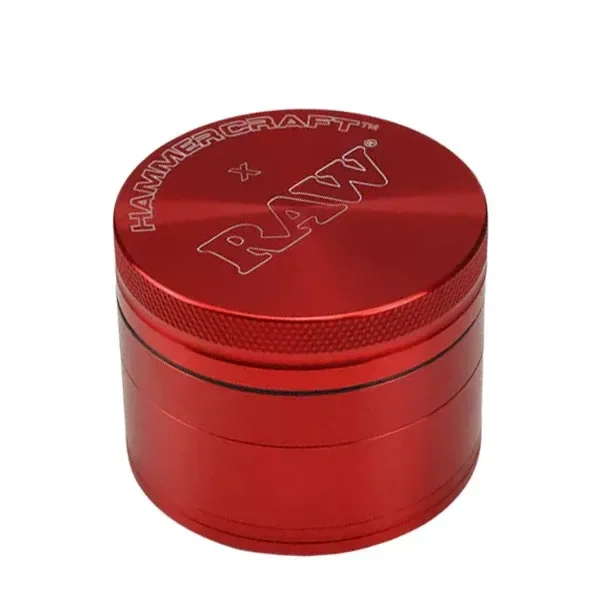 Grinder rojo cilíndrico visto en perspectiva, con bordes estriados y los nombres HAMMERCRAFT y RAW grabados en la tapa.