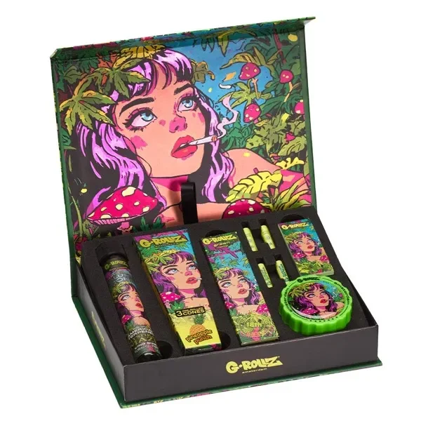 Caja abierta G-Rollz Mystikal Maze con accesorios decorados, grinder verde e ilustración de una mujer entre hojas y setas en la tapa. Caja abierta G-Rollz Mystikal Maze con accesorios decorados, grinder verde e ilustración de una mujer entre hojas y setas en la tapa.
