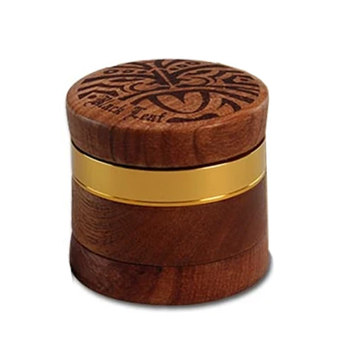 Grinder de madera Maori cerrado, de forma cilíndrica, con una franja dorada y un motivo oscuro grabado en la tapa, sobre fondo blanco.