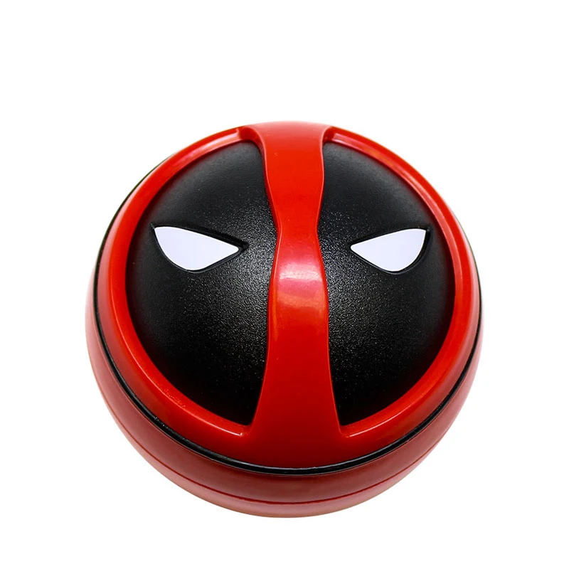 Grinder circular visto desde arriba y en ángulo, con tapa roja y negra decorada con los ojos blancos de la máscara de Deadpool.