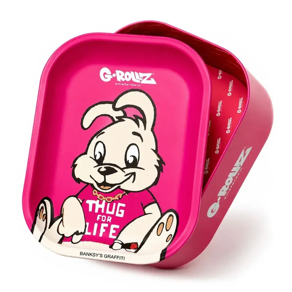 Bandeja y caja rosa Thug For Life, con la caja abierta detrás y un conejo dibujado en la bandeja que viste una camiseta con ese texto. Bandeja y caja rosa Thug For Life, con la caja abierta detrás y un conejo dibujado en la bandeja que viste una camiseta con ese texto.