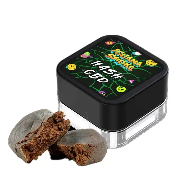 Envase cuadrado de Hash CBD Iguana Smoke Nepal Cream con tapa negra decorada y dos trozos marrones abiertos delante.