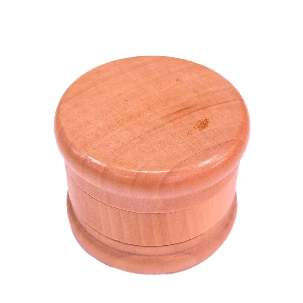 Grinder de madera cerrado, de forma cilíndrica, con tapa redonda lisa, bordes redondeados y vetas visibles sobre fondo blanco.