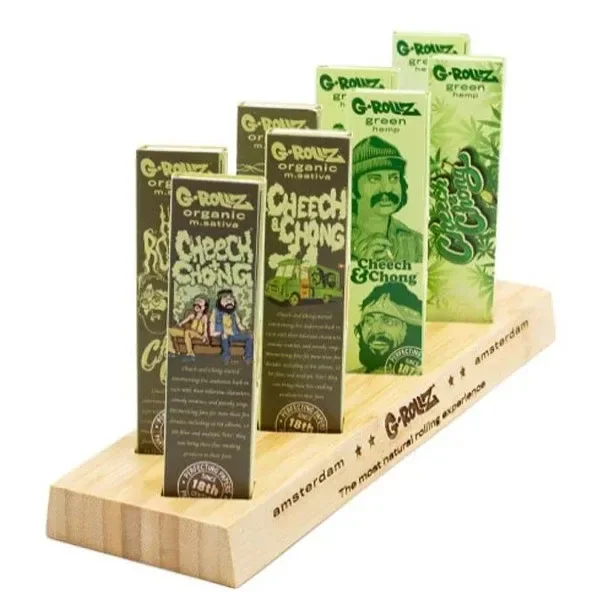 Expositor Bamboo G-Rollz con base de madera y varios libritos de papel de fumar en tonos verdes, con diseños de Cheech y Chong.