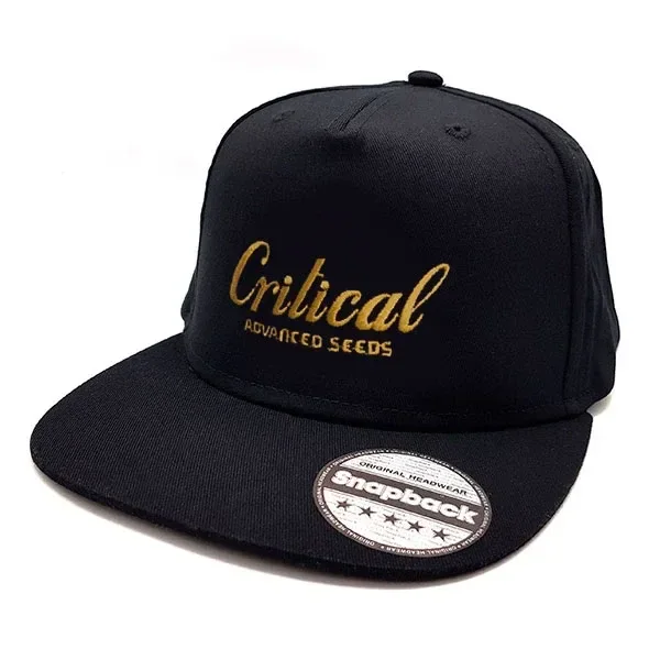Gorra negra de visera plana con bordado dorado «Critical Advanced Seeds» y pegatina circular sobre la visera.
