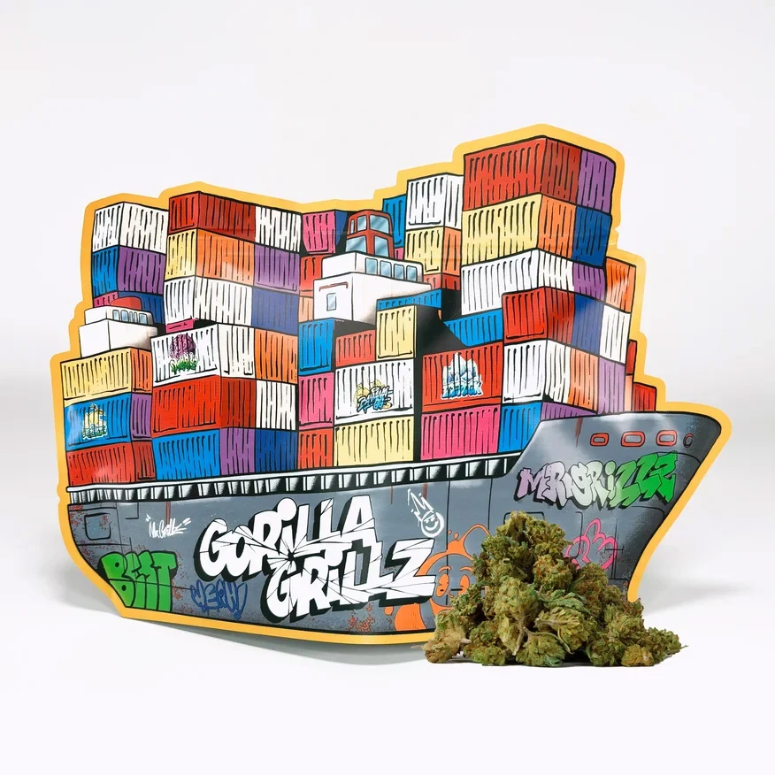 Envase Gorilla Grillz con forma de barco, contenedores multicolores y grafitis, con varios cogollos delante sobre fondo blanco.