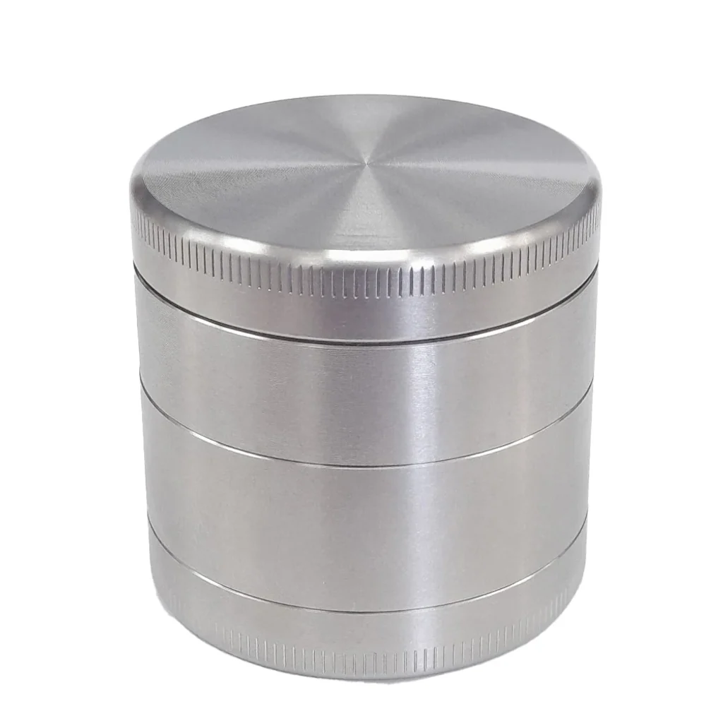 Grinder polinizador plateado y cilíndrico, cerrado, con varios cuerpos superpuestos y bordes estriados sobre fondo blanco.
