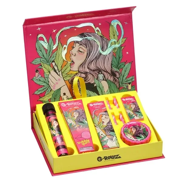 Caja regalo G-Rollz abierta con interior amarillo, accesorios ilustrados y tapa rosa con una mujer entre hojas y humo. Caja regalo G-Rollz abierta con interior amarillo, accesorios ilustrados y tapa rosa con una mujer entre hojas y humo.
