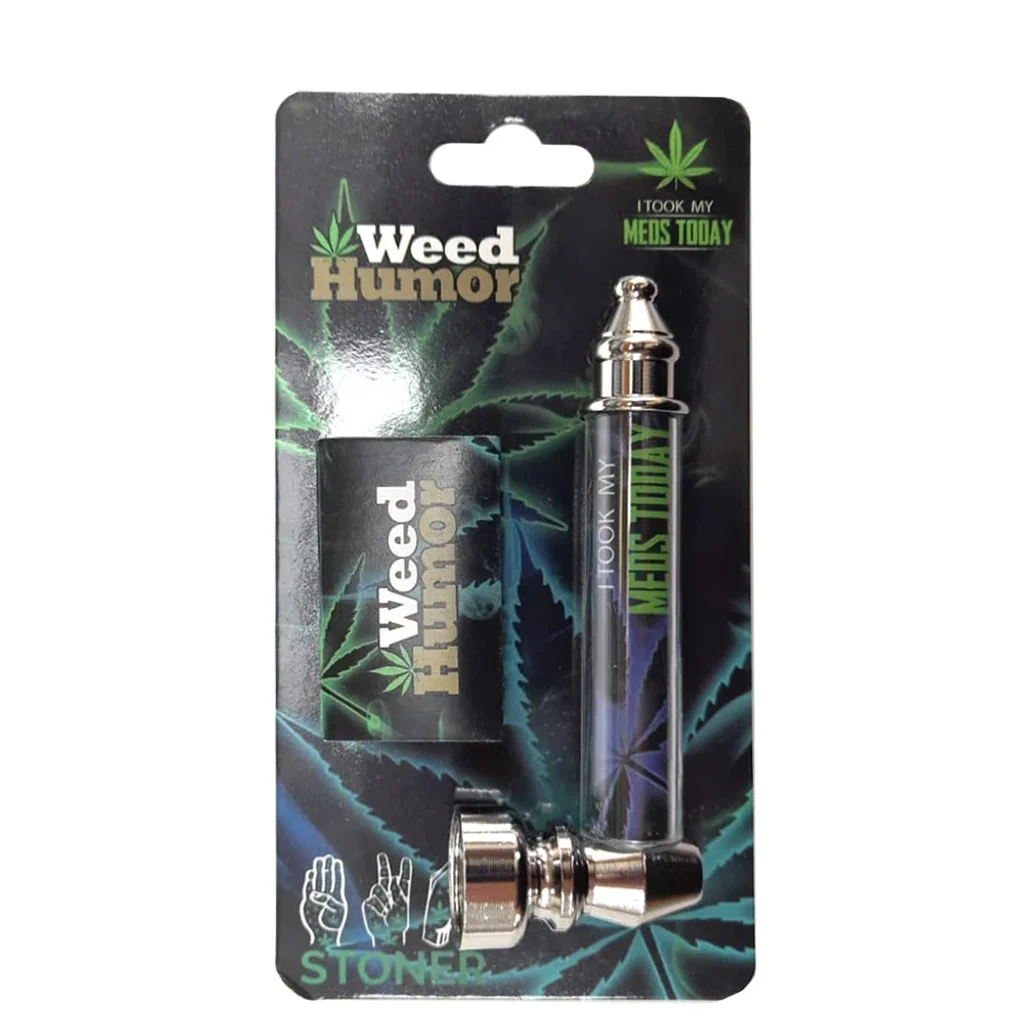 Pipa Weed Humor en blíster, con tubo decorado, extremos metálicos brillantes y cazoleta lateral, sobre cartón con hojas de cannabis.