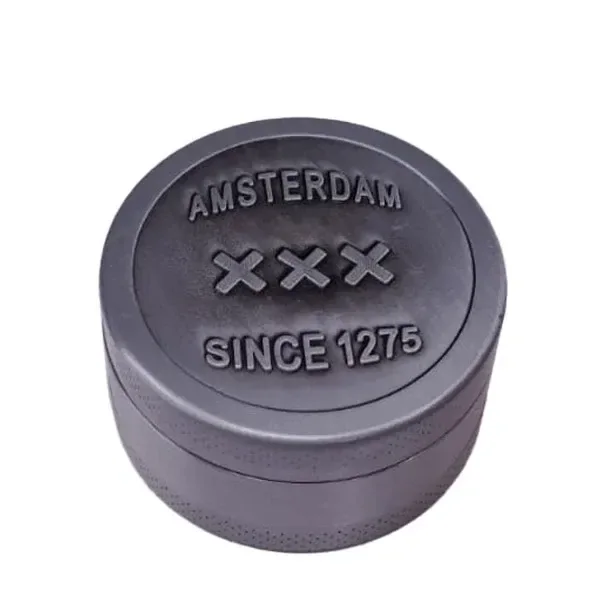 Grinder circular gris visto en perspectiva, con bordes texturizados y tapa grabada con «AMSTERDAM», tres cruces y «SINCE 1275».