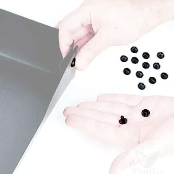 Manos que sujetan pequeños remaches negros junto al borde de una bandeja gris, con varias piezas sueltas sobre fondo blanco. Manos que sujetan pequeños remaches negros junto al borde de una bandeja gris, con varias piezas sueltas sobre fondo blanco.