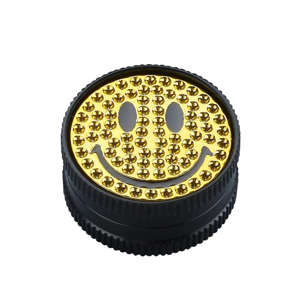Grinder Gold Smile cerrado, con cuerpo negro estriado y tapa dorada con cara sonriente y pequeños adornos brillantes.
