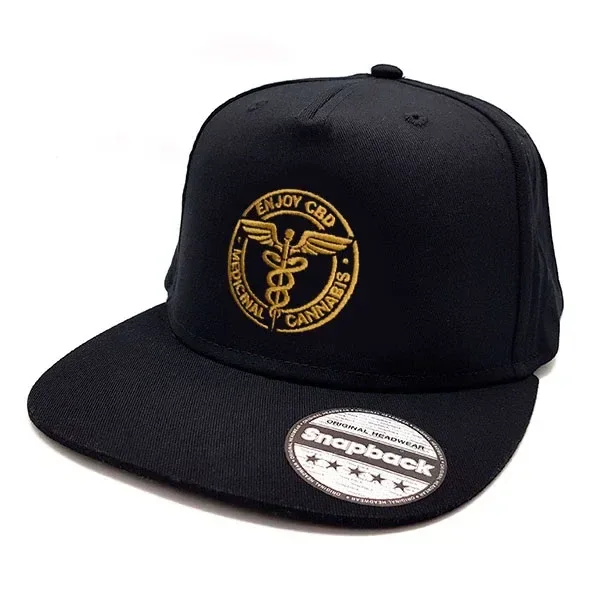 Gorra negra Enjoy CBD con visera plana, emblema circular bordado en dorado y pegatina Snapback sobre la visera.