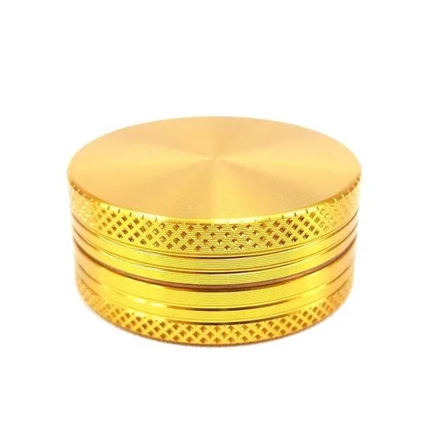 Grinder Gold de metal dorado, cerrado y visto en perspectiva, con tapa lisa y bordes de agarre con relieve romboidal.