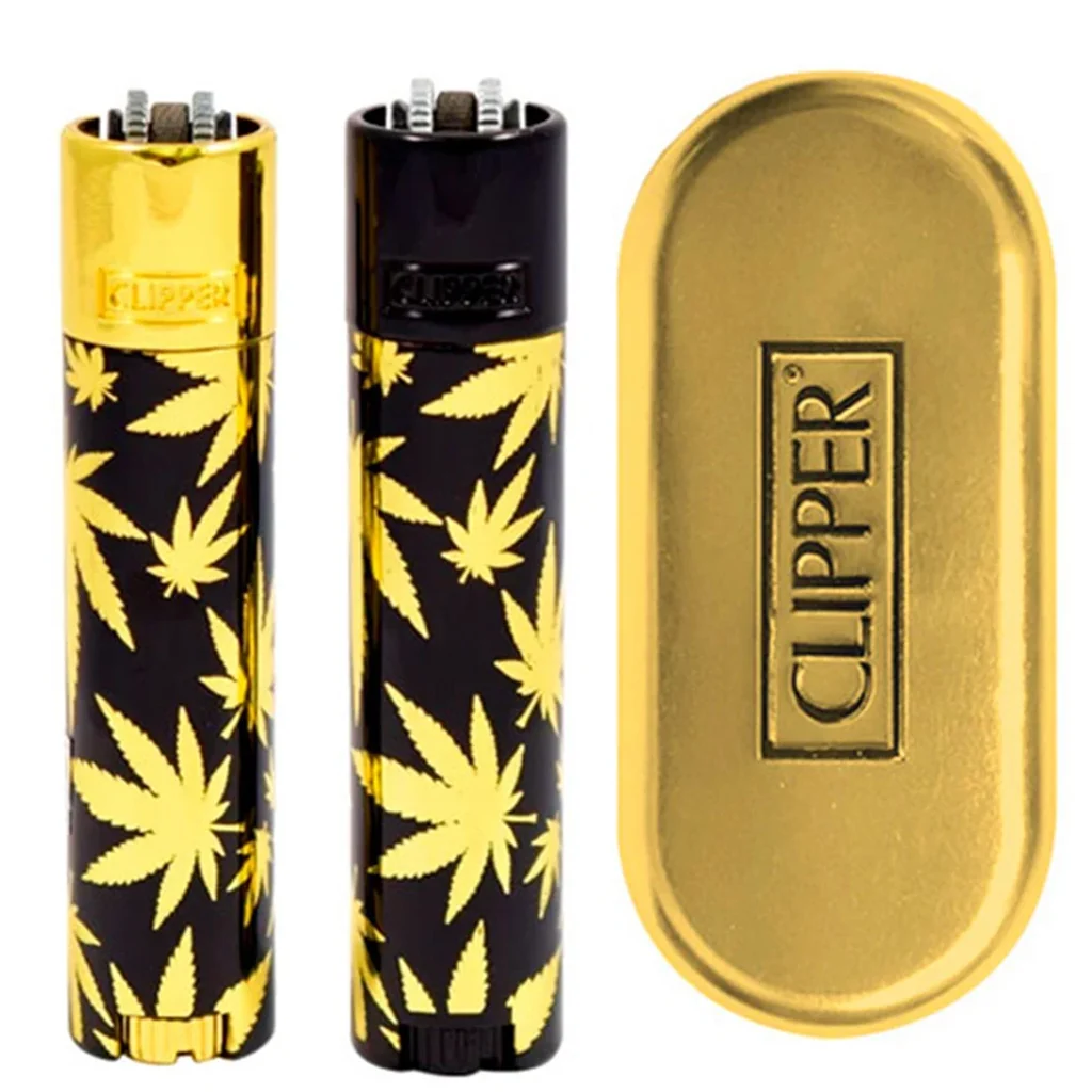 Mecheros Clipper con hojas doradas sobre fondo negro, acabados superiores dorado y negro, junto a un estuche dorado con logotipo.