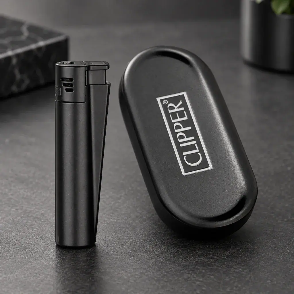 Encendedor Clipper negro de pie junto a un estuche ovalado negro con el logotipo de la marca, sobre una superficie oscura.