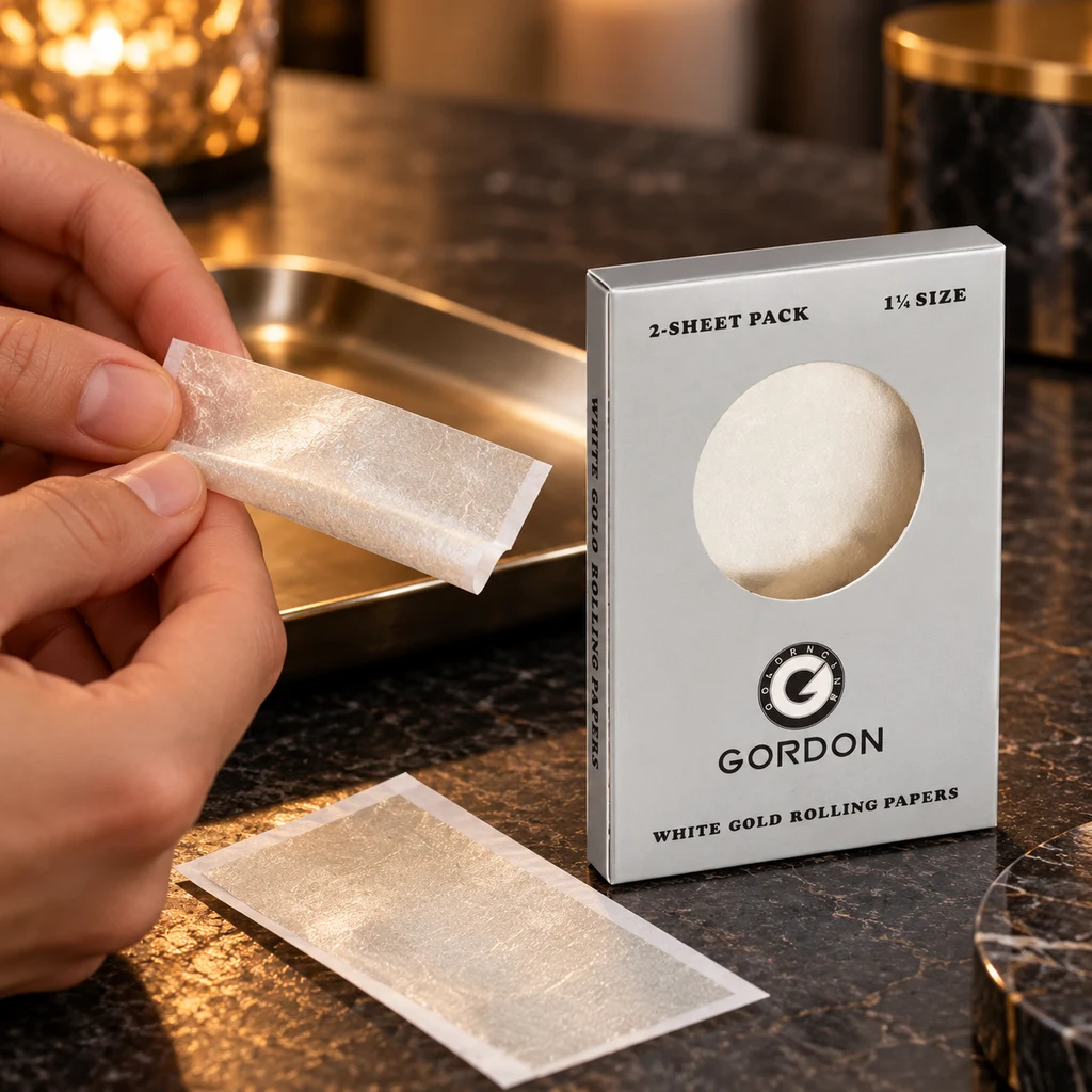 Manos sostienen un papel de liar White Gold de brillo dorado junto a su caja Gordon, rotulada «2-sheet pack» y «1¼ size».