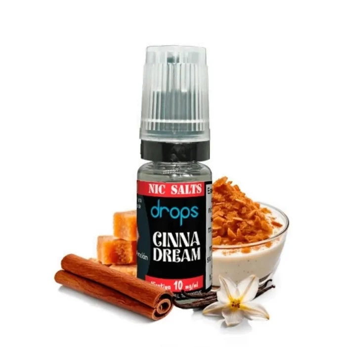 Frasco Drops Salts Cinnadream con tapón transparente, junto a ramas de canela, un cuenco con cereales y una flor de vainilla.