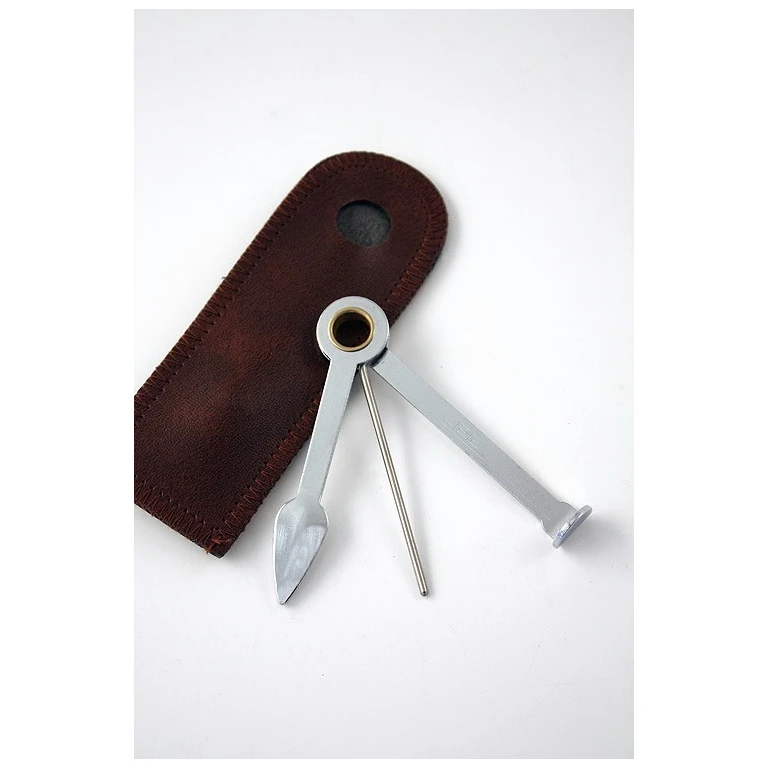 Atacapipas metálico desplegado con tres accesorios: cucharilla, varilla y prensador, junto a una funda marrón con costuras visibles.