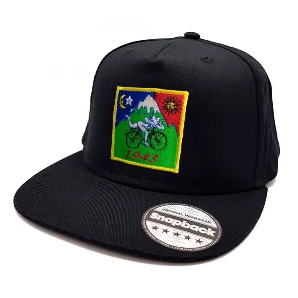 Gorra negra de visera plana con bordado multicolor de un ciclista, montañas, sol y luna, el número 1943 y una pegatina en la visera.
