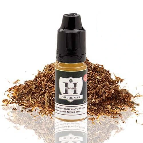 Frasco de Herrera Churdinas con tapón negro y etiqueta blanca, delante de un montón de tabaco picado sobre una superficie reflectante.