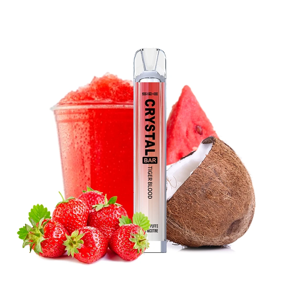 Vaper SKE Crystal Bar Tiger Blood en posición vertical, junto a fresas, medio coco, una rodaja de sandía y un granizado rojo. Vaper SKE Crystal Bar Tiger Blood en posición vertical, junto a fresas, medio coco, una rodaja de sandía y un granizado rojo.
