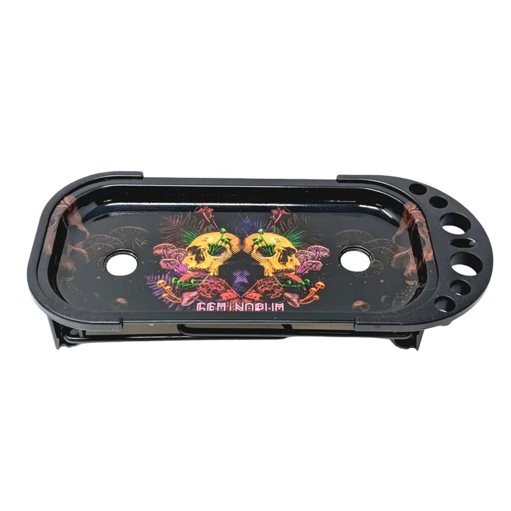 Bandeja negra alargada con dos calaveras amarillas enfrentadas, motivos multicolor y orificios circulares en la base y el lateral derecho.