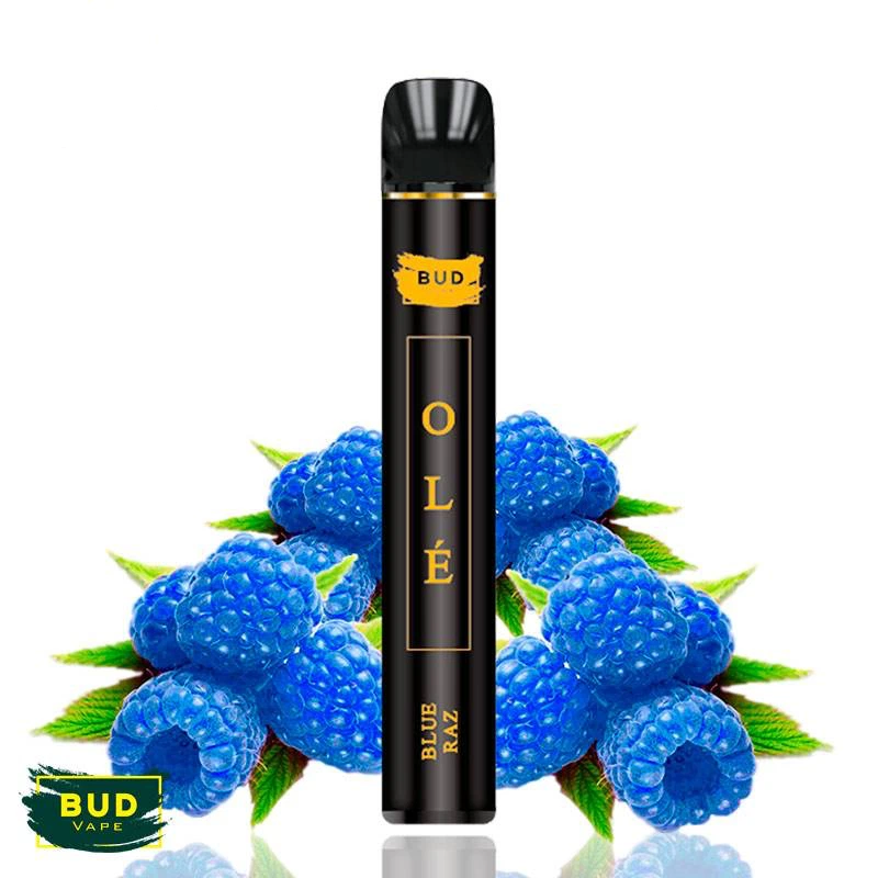 Pod negro Blue Razz Olé de Bud Vape, con letras doradas, rodeado de frambuesas azules y hojas verdes sobre fondo blanco.