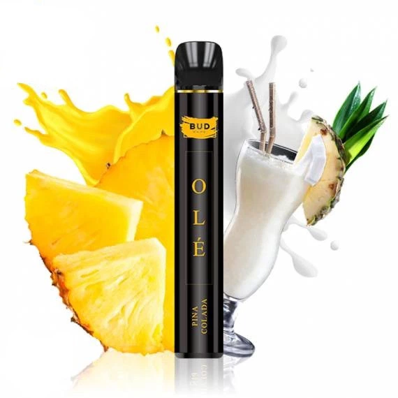 Vapeador negro Bud Vape Olé Piña Colada con letras doradas, junto a trozos de piña y una copa con bebida blanca y pajitas.