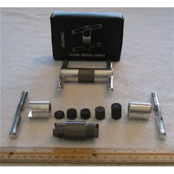 Prensa manual Super Herbal Press montada y desmontada, con piezas cilíndricas, barras de giro, caja negra y una regla delante.