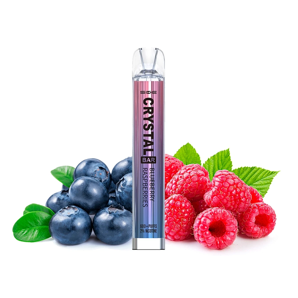 Vaper SKE Crystal Bar Blueberry Raspberry con cuerpo rosa y azul y boquilla transparente, rodeado de arándanos y frambuesas. Vaper SKE Crystal Bar Blueberry Raspberry con cuerpo rosa y azul y boquilla transparente, rodeado de arándanos y frambuesas.