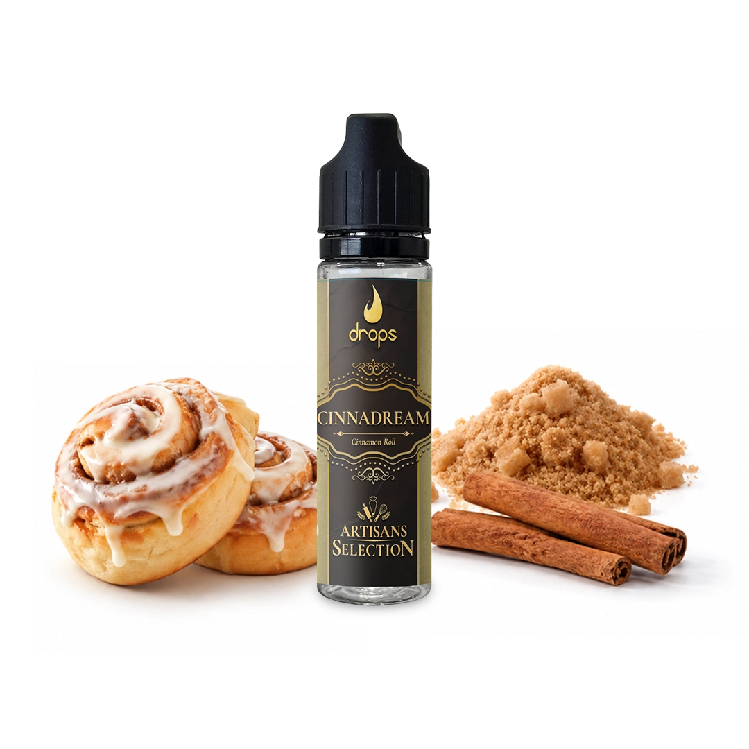 Bote de Drops Cinnadream con tapón negro y etiqueta dorada, junto a rollos glaseados, ramas de canela y azúcar moreno.