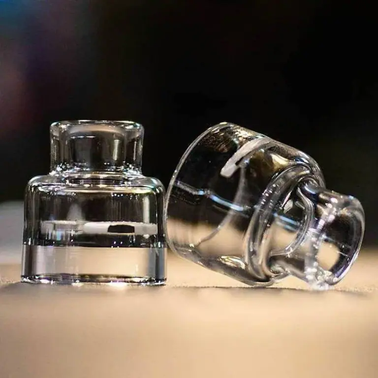 Tapas transparentes RECOIL Trinity Glass Cap con boquilla corta, una en posición vertical y otra tumbada sobre una superficie clara.