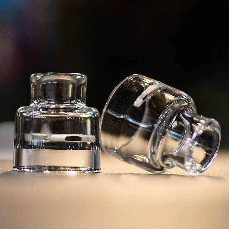 Tapas transparentes RECOIL Trinity Glass Cap con boquilla corta, una en posición vertical y otra tumbada sobre una superficie clara.