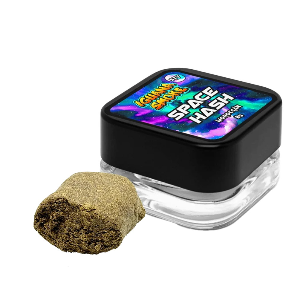 Tarro de Space Hash de Iguana Smoke con tapa negra y etiqueta multicolor, junto a un trozo dorado de superficie granulada sobre fondo negro.