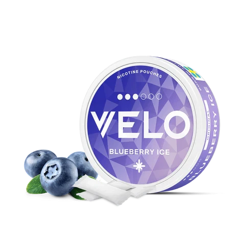 Envase redondo de VELO Blueberry Ice con etiqueta violeta, junto a arándanos y bolsas blancas sobre fondo negro. Envase redondo de VELO Blueberry Ice con etiqueta violeta, junto a arándanos y bolsas blancas sobre fondo negro.