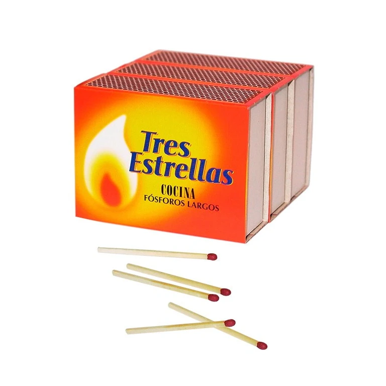Cajas de fósforos Tres Estrellas con frontal naranja y superficies de encendido, junto a varias cerillas largas de cabeza roja.