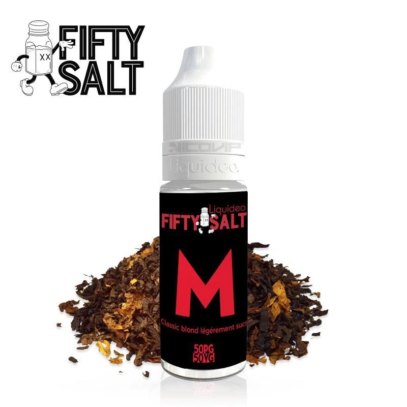 Frasco de Le M Fifty Salt con tapón blanco, etiqueta negra con una gran M roja y texto 50PG/50VG, delante de tabaco suelto.