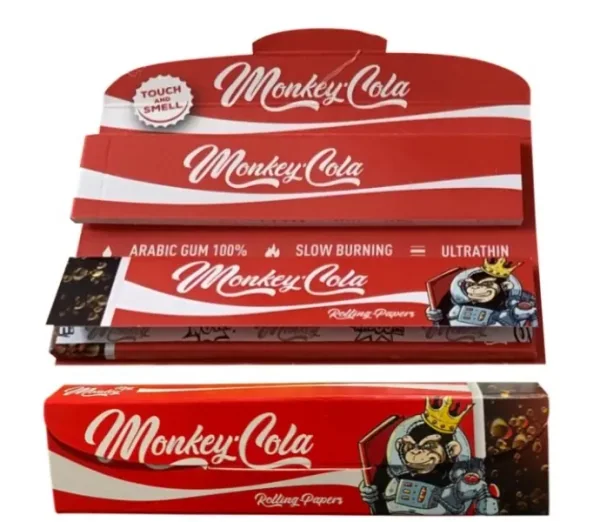 Expositor abierto y librillo rojo de papel Monkey Cola, con franjas blancas, letras cursivas y un mono coronado vestido de astronauta.