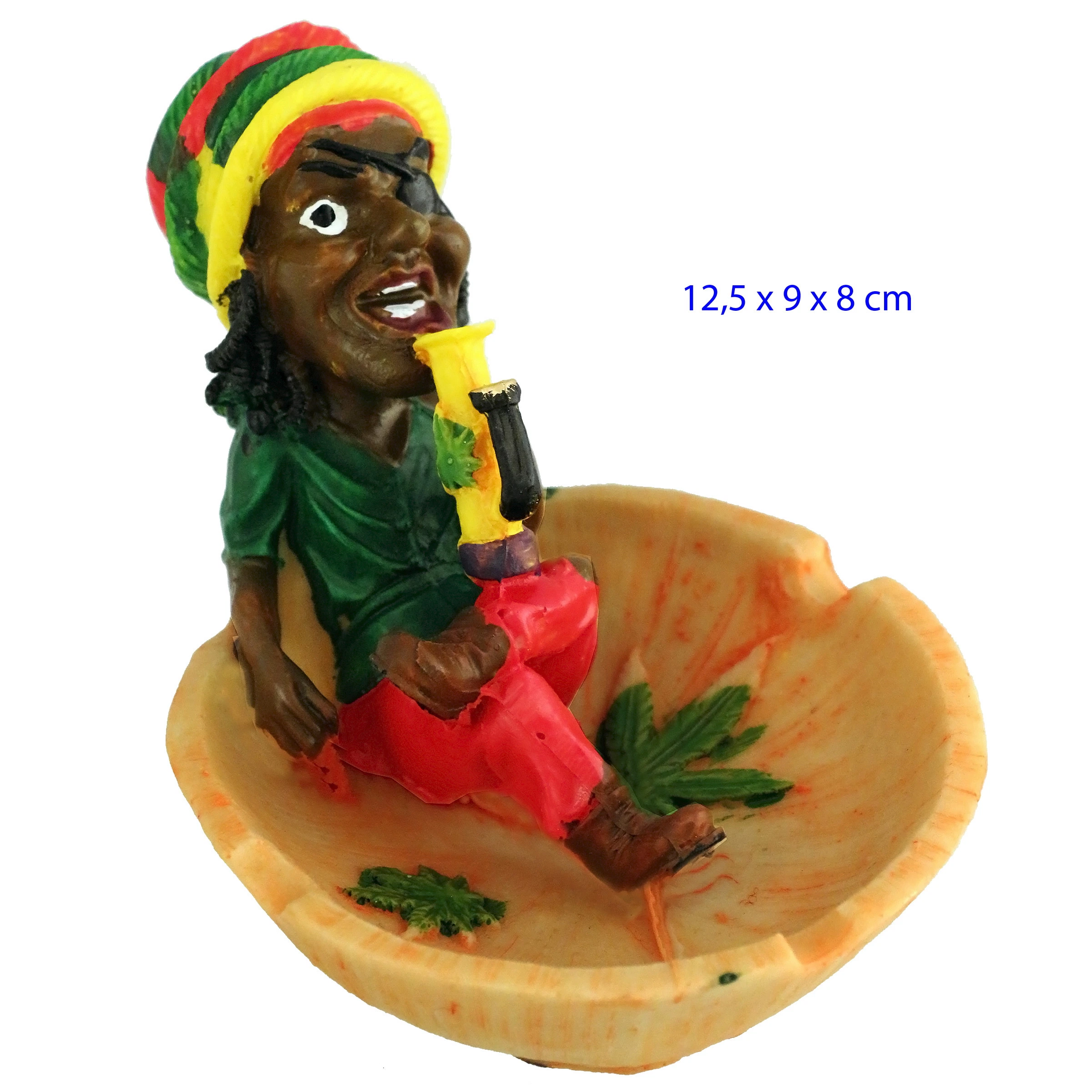 Cenicero de mesa con figura rasta sentada sosteniendo un bong amarillo, gorro multicolor y hojas verdes decorativas en la base.